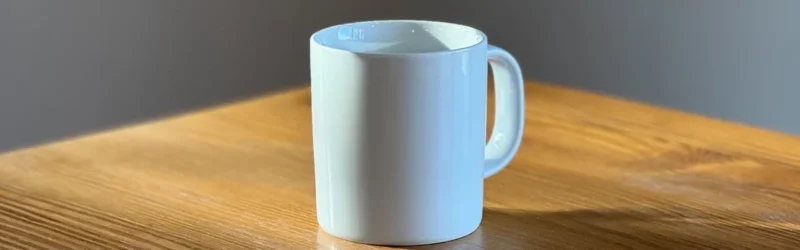 木のテーブルに置かれたUCHIDA COFFEEの白いマグカップと注ぎ込む朝日